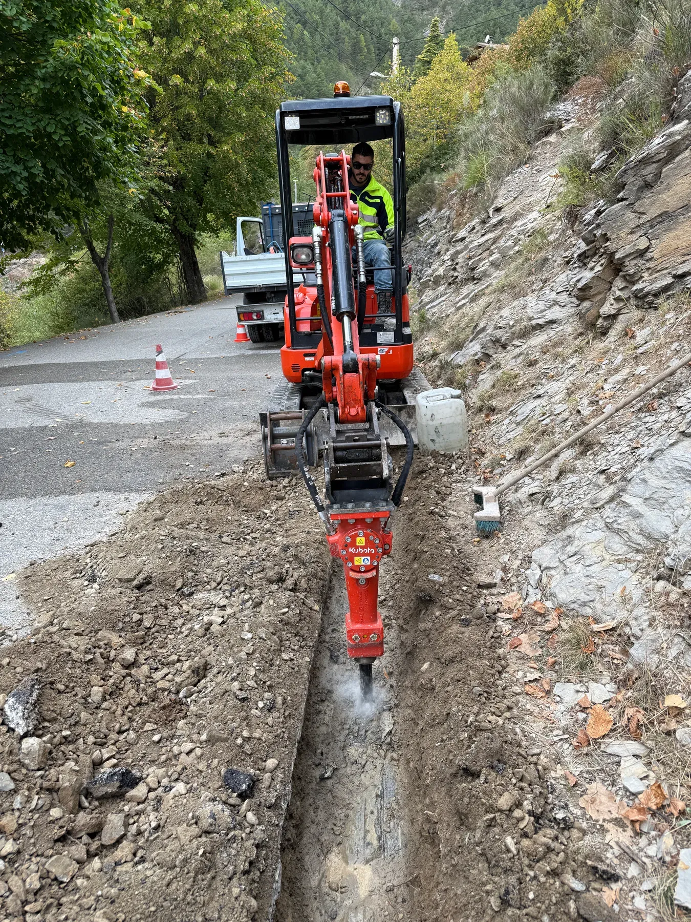 Mini-pelle équipée d'un brise-roche réalisant une tranchée pour la fibre à Venanson