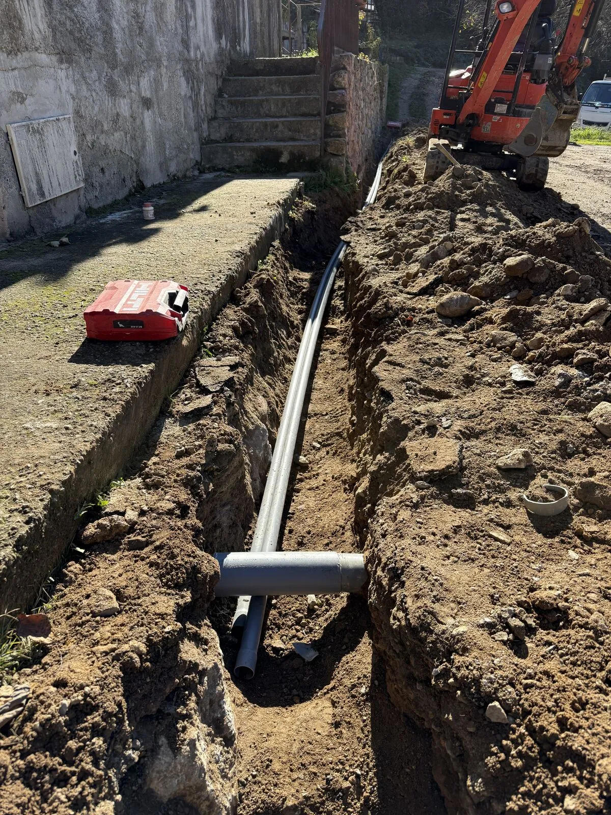 Tranchée de raccordement le long de l'habitation : fourreaux posés et manchonnés, mini-pelle en action